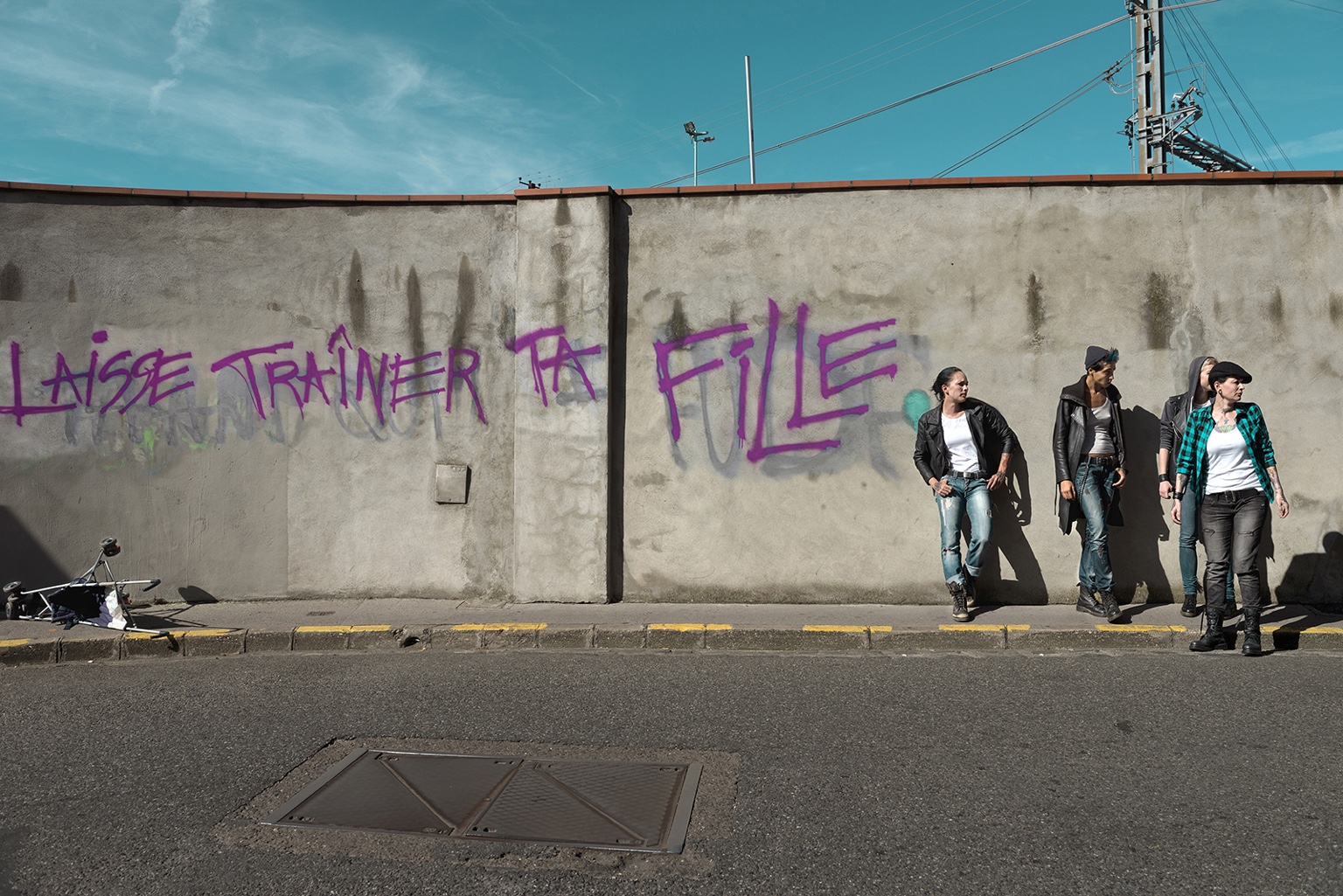 Trois femmes de la série Benzine Cyprine devant un mur couvert de graffiti